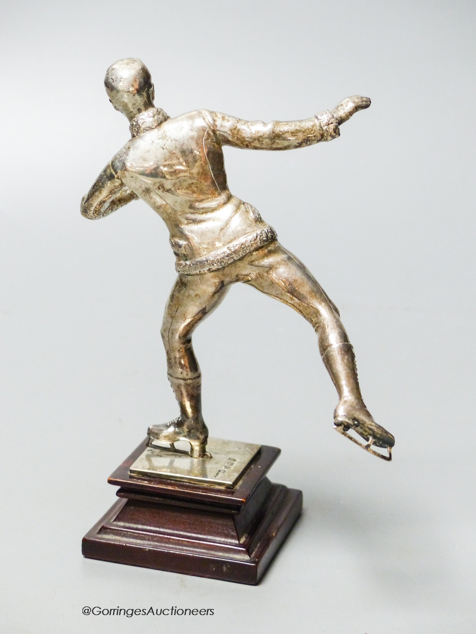 An Edwardian silver miniature model of an ice skater, Elkington & Co Ltd?, London, 1904, on a wooden plinth base, skater 12cm, gross weight 10oz.